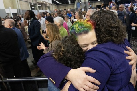 Three people hugging. One of the people has rainbow colored hair.