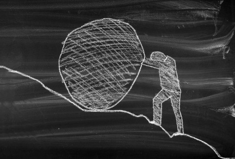 person pushing a boulder up a hill