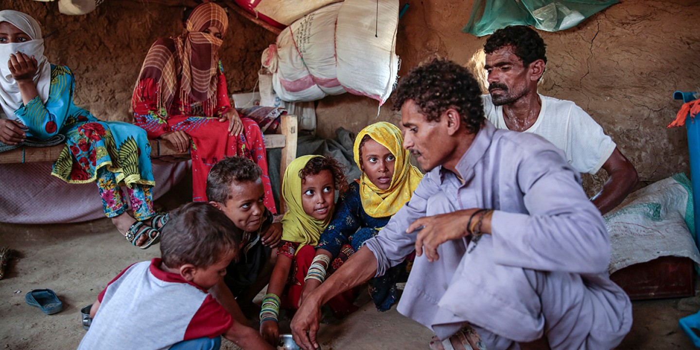 adults and children crouching to eat Halas from a common bowl